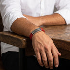 Pulsera siendo modelada por hombre que posa su mano sobre una mesa, la pulsera es de cuero con placa metalica
