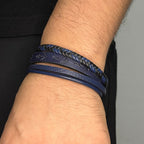 Pulsera de cuero sintético para hombre en color azul y negro, con grabado de anclas negras, formada por cuatro tiras: una trenzada, una lisa, una delgada y una con diseño náutico sobre fondo azul