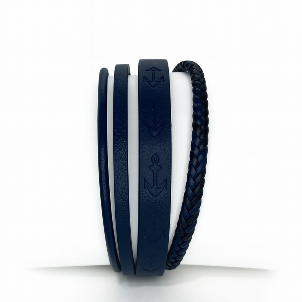 Pulsera de cuero sintético para hombre en color negro y rojo, con grabado de anclas negras, formada por cuatro tiras: una trenzada, una lisa, una delgada y una con diseño náutico sobre fondo azul.