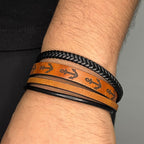 Pulsera de cuero sintético para hombre en color marron y negro, con grabado de anclas negras, formada por cuatro tiras: una trenzada, una lisa, una delgada y una con diseño náutico sobre fondo marron