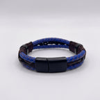 Broche magnético negro mate de acero inoxidable en pulsera de cuero azul para hombre, flanqueado por separadores oscuros y tejido artesanal.