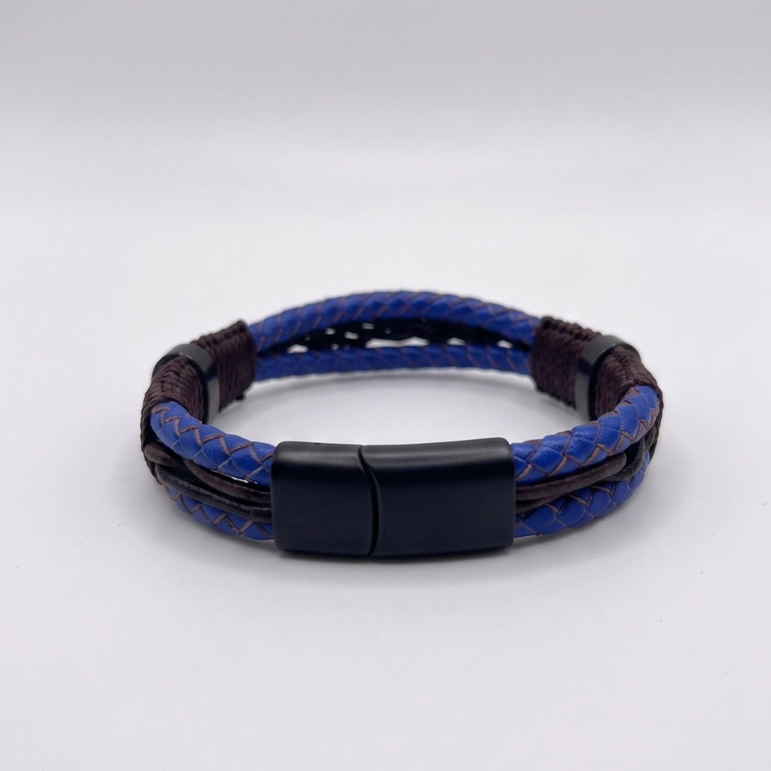 Broche magnético negro mate de acero inoxidable en pulsera de cuero azul para hombre, flanqueado por separadores oscuros y tejido artesanal.