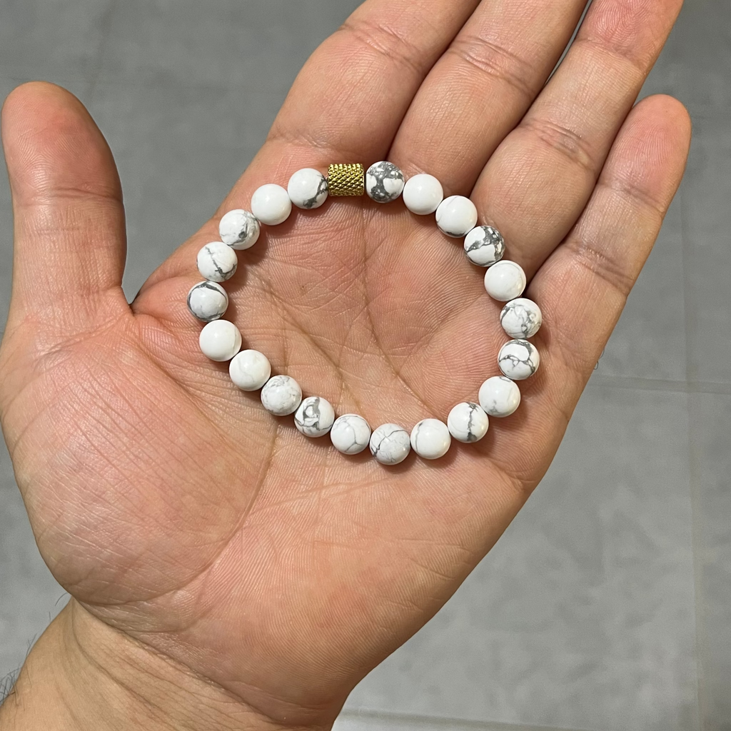 Pulsera o manilla sobre una mano, la puslera es de tipo howlita o pino blanco para hombre krv colombia