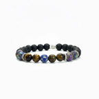Pulsera elástica para hombre elaborada con cuentas de piedra volcánica negra, ojo de tigre dorado, soladita y piedras iridiscentes multicolor, con separadores metálicos en acero inoxidable, sobre fondo neutro gris claro. Vista horizontal