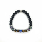 Pulsera elástica para hombre elaborada con cuentas de piedra volcánica negra, ojo de tigre dorado, soladita y piedras iridiscentes multicolor, con separadores metálicos en acero inoxidable, sobre fondo neutro gris claro. Vista superior