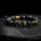 Pulsera de pirita natural y piedra volcánica para hombre con detalle en acero dorado, fondo de piedra negra
